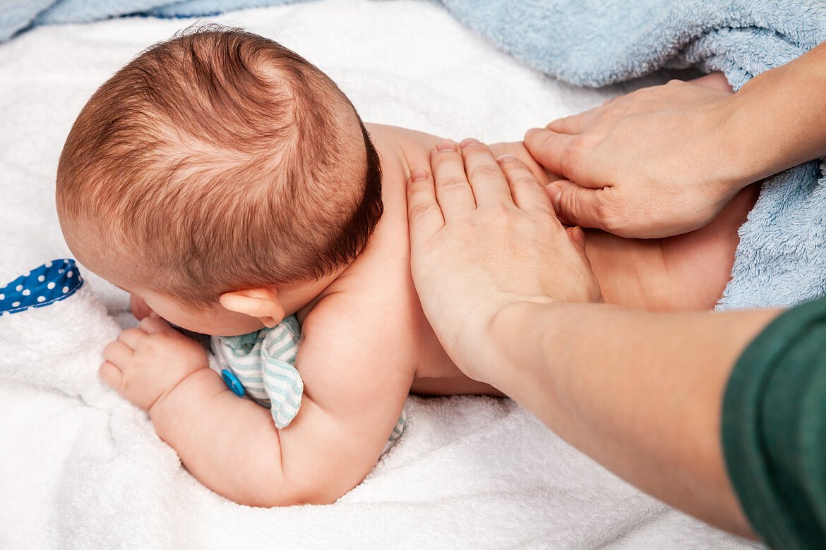 Fünf Monate altes Kleinkind liegt auf dem Bauch. Osteopathie-Behandlung am Rücken. Hande des Therapeuten auf dem Baby.