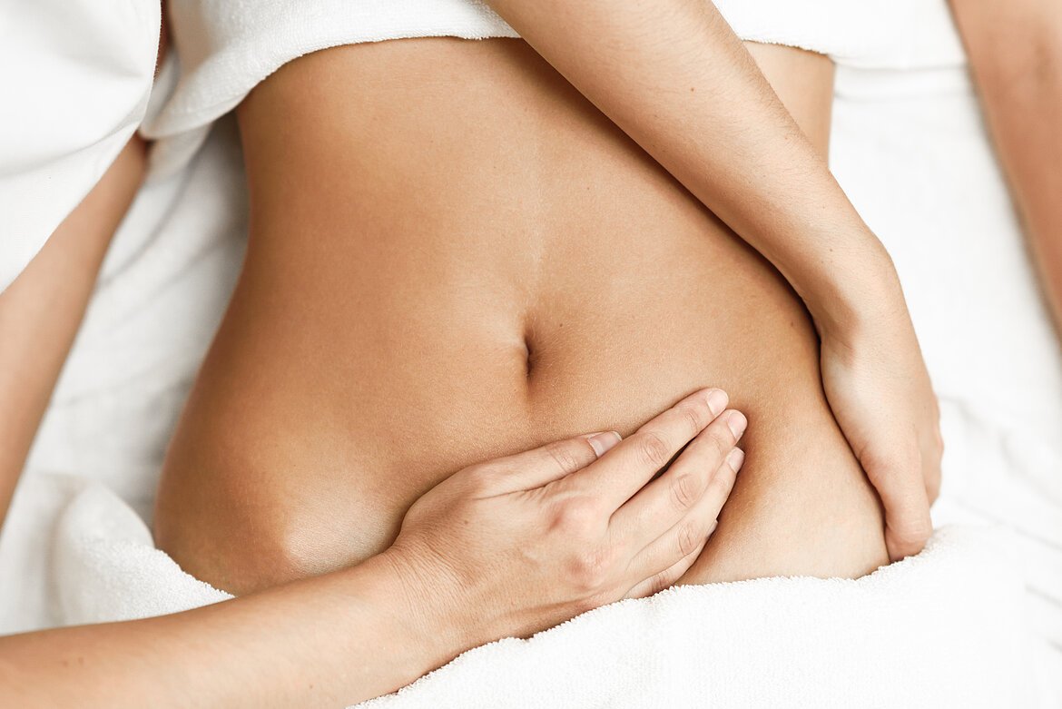 Osteopathische Behandlung, Hände des Osteopathen liegen auf Bauch und Becken der Patientin.