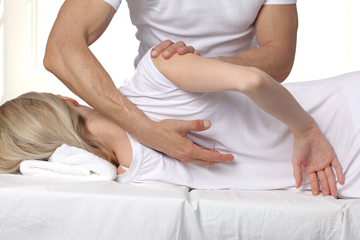 Osteopathische Behandlung einer Frau. Osteopath drückt gegen Arm und Rücken der Patientin.
